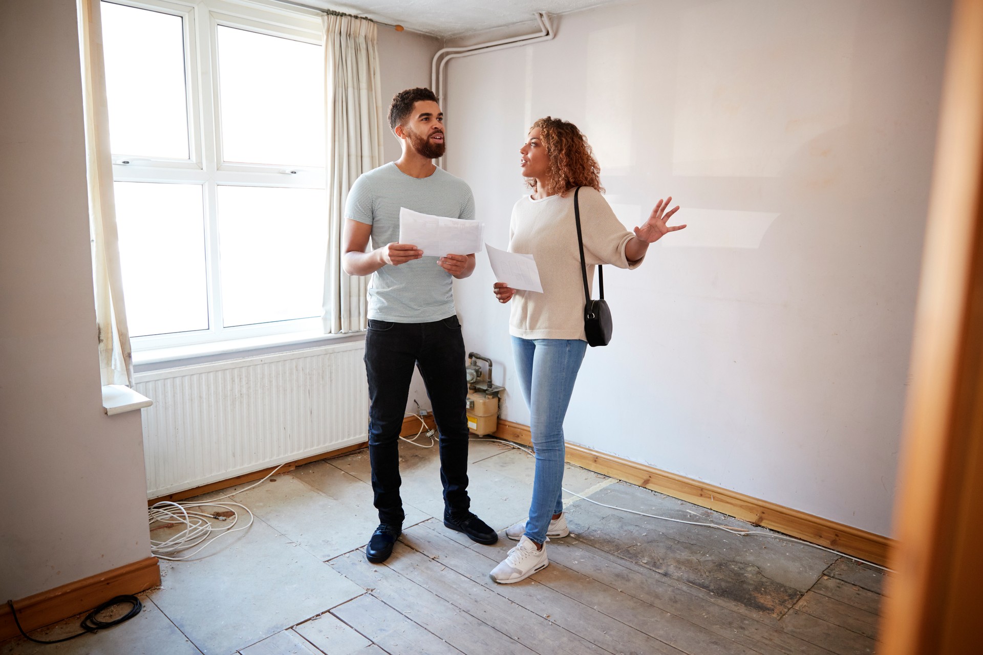 Couple Buying House For First Time Looking At House Survey In Room To Be Renovated